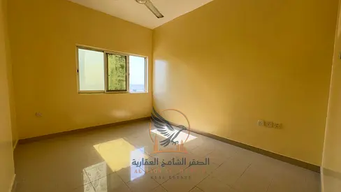 Two-bedroom apartment with a living room in Ajman Industrial Area 2, behind Emirates Markets, with a balcony and two bathrooms.